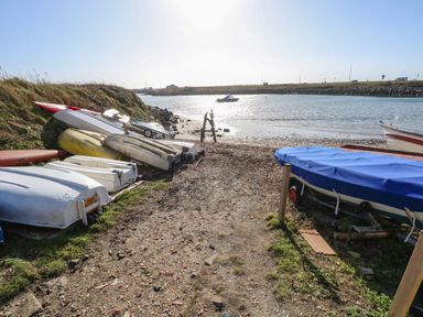 Small boats stored on the shore near a body of water with a boat floating in the water at Sandpiper in Weymouth