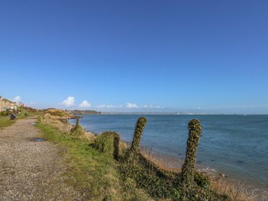 A coastal pathway with grassy areas and houses on one side and the sea on the other at Sandpiper Weymouth