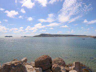A view of a calm sea with rocks in the foreground and a hilly coastline in the distance at Sandpiper Weymouth