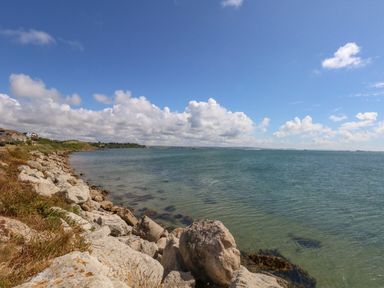 A rocky shoreline with water and houses in the background at Sandpiper in Weymouth