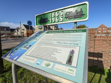 An information board about the Rodwell Trail next to a sign with years 1865 and 1965 in a residential area in Weymouth