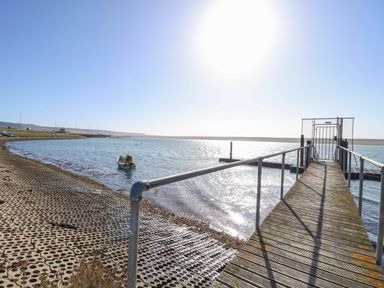 A metal railing pier with gate extending over water near a shoreline with a small boat at Sandpiper in Weymouth
