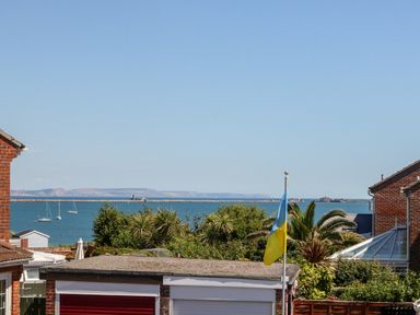 A sea view with sailboats and distant land seen between houses and trees at Sandpiper in Weymouth