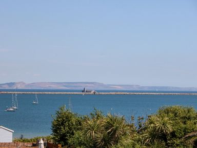 A coastal view with sailboats on water and a breakwater with buildings in the distance at Sandpiper in Weymouth