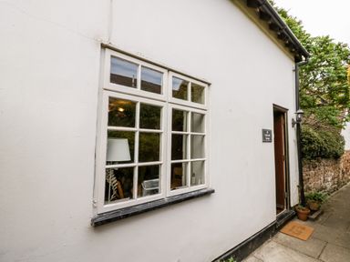 Exterior side wall of a white cottage with a window and an open door showing a welcome mat at Hock-tide Cottage in Kenilworth