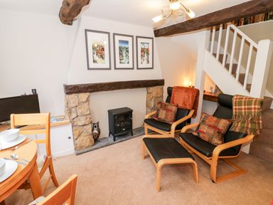 A sitting area with chairs a small stove and dining table near stairs at Hock-tide Cottage in Kenilworth
