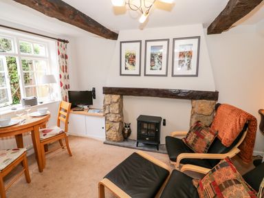 A living room with wooden chairs a small table a fireplace with a stove and framed pictures on the wall at Hock-tide Cottage in Kenilworth