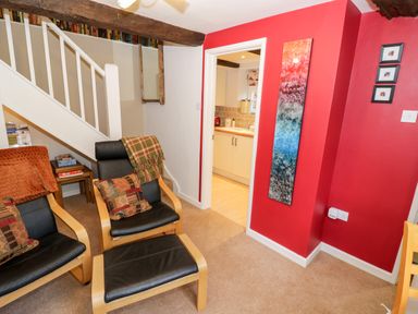 A sitting area with two chairs and a footrest near a staircase and an entrance to a kitchen at Hock-tide Cottage in Kenilworth