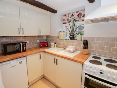 A kitchen with cream cabinets a white sink a red toaster a red microwave and a white stove at Hock-tide Cottage in Kenilworth
