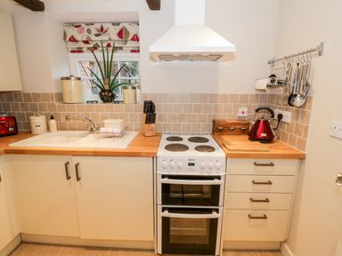 A kitchen with a sink stove and kettle on wooden countertops at Hock-tide Cottage in Kenilworth