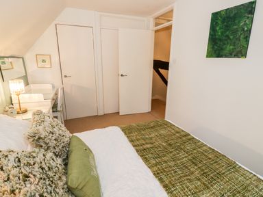 A bedroom with a bed green pillows a white dresser with lamp and mirror and two white doors at Hock-tide Cottage in Kenilworth