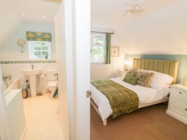 A bedroom with a bed and side tables next to a bathroom with a sink toilet and bathtub at Hock-tide Cottage in Kenilworth