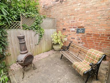 A small outdoor patio with a bench and blanket next to a vintage stove and potted plant at Hock-tide Cottage Kenilworth