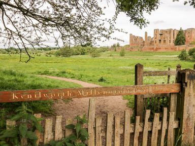 A footpath with a wooden sign reading Kenilworth Millennium Trail and castle ruins in the background at Hock-tide Cottage in Kenilworth