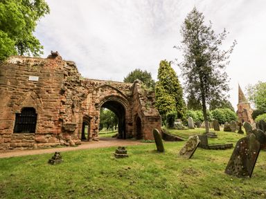 An outdoor scene with old stone ruins surrounded by grass trees and gravestones at Hock-tide Cottage in Kenilworth