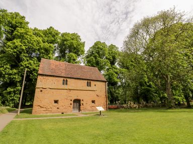 An old stone building with a tiled roof surrounded by grass and trees at Hock-tide Cottage in Kenilworth