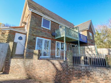 The exterior of a two-story brick house with balconies and metal fencing at Castle Cove Cottage in Weymouth