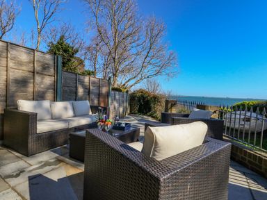 An outdoor patio with wicker seating and a table overlooking the sea at Castle Cove Cottage in Weymouth
