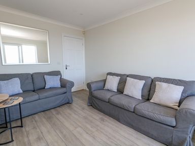 A living room with two grey sofas with cushions and a mirror on the wall at Castle Cove Cottage in Weymouth