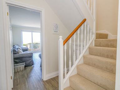 A carpeted staircase next to a hallway with wood flooring leading to a living room with a sofa and sliding glass doors at Castle Cove Cottage in Weymouth