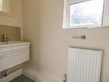 A small bathroom with a sink cabinet radiator and a frosted window at Castle Cove Cottage in Weymouth