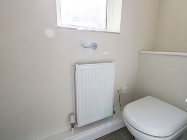 A small bathroom with a white radiator below a window and a white toilet in the corner at Castle Cove Cottage in Weymouth