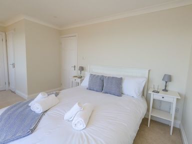 A bedroom with a white bed, two bedside tables with lamps, and rolled towels on the bed at Castle Cove Cottage in Weymouth