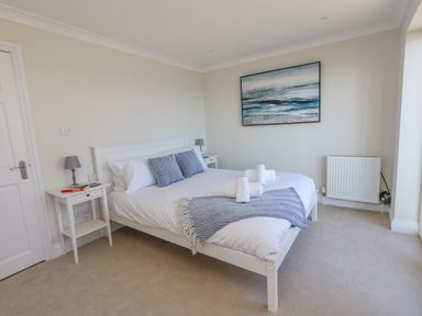 A bedroom with a white bed and side tables with lamps and a painting on the wall at Castle Cove Cottage in Weymouth