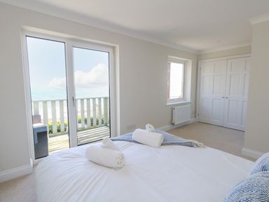 A bedroom with a bed and rolled towels near glass doors opening to a balcony at Castle Cove Cottage in Weymouth