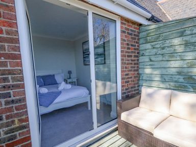A bedroom with a bed and nightstand seen through glass sliding doors opening to a patio with a wicker sofa at Castle Cove Cottage in Weymouth