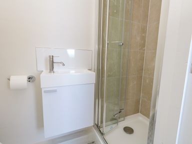 A bathroom with a white sink cabinet and a glass shower enclosure with beige tiled walls at Castle Cove Cottage in Weymouth