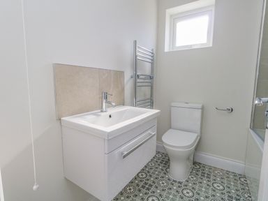 A bathroom with a sink cabinet toilet window and patterned tile floor at Castle Cove Cottage in Weymouth