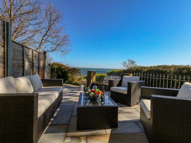 An outdoor patio with rattan sofa and chairs around a glass coffee table with a view of the sea at Castle Cove Cottage in Weymouth