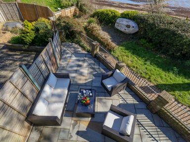 An outdoor patio area with a sofa table and two chairs next to a garden and beach at Castle Cove Cottage in Weymouth