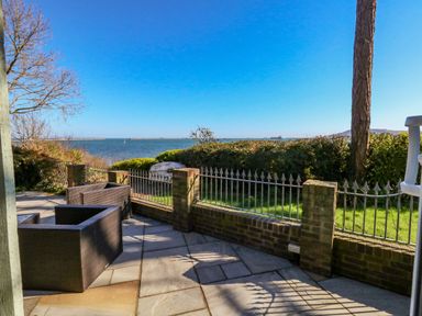 A patio with chairs overlooking a fenced garden and a body of water at Castle Cove Cottage in Weymouth