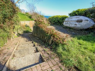A set of outdoor concrete stairs surrounded by shrubs and greenery next to an upturned small boat at Castle Cove Cottage in Weymouth