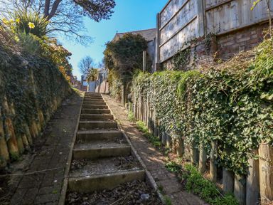 An outdoor staircase with plants and fences on either side under a clear sky at Castle Cove Cottage in Weymouth