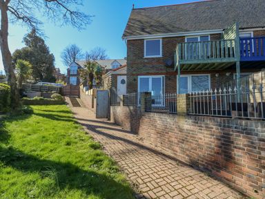 A brick house with a driveway and grass lawn next to it at Castle Cove Cottage in Weymouth