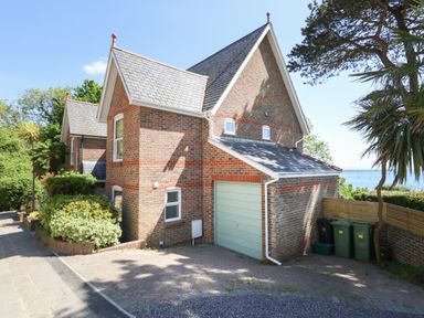 A brick house with a garage and trees by the roadside at Castle Cove Cottage in Weymouth