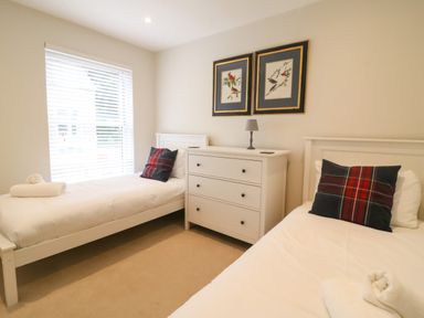 A bedroom with two single beds with plaid pillows a white chest of drawers and framed bird pictures on the wall at Castle Cove Cottage in Weymouth