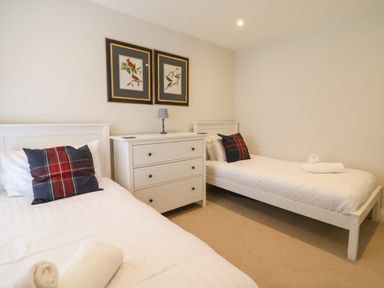 A bedroom with two single beds a white dresser with a lamp and framed bird pictures at Castle Cove Cottage Weymouth