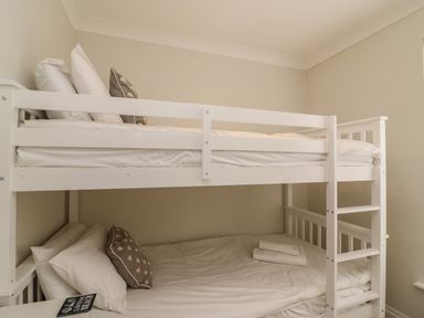 A bedroom with a white bunk bed and white bedding at Castle Cove Cottage in Weymouth