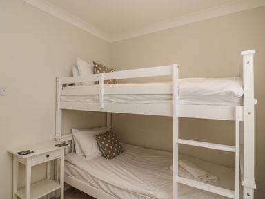 A bedroom with a white bunk bed and a small white side table at Castle Cove Cottage in Weymouth
