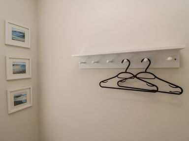 A wall with a white coat rack holding two black hangers and three framed pictures at Castle Cove Cottage in Weymouth