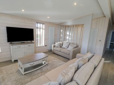 A living room with two sofas a coffee table a cabinet with a television and a large window at No 27 The Crab Pot in Runswick Bay near Staithes