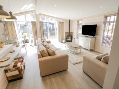 A living room with beige sofas a coffee table a TV on a cabinet and large windows at No 27 The Crab Pot in Runswick Bay near Staithes