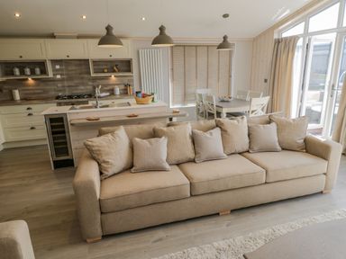A living room with a beige sofa and an open kitchen with dining table and chairs at No 27 The Crab Pot in Runswick Bay near Staithes