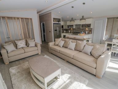 A living room with two beige sofas a coffee table and a rug near a kitchen with a refrigerator and dining table at No 27 The Crab Pot Runswick Bay near Staithes