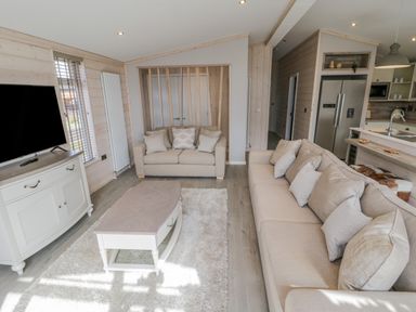 A living room with beige sofas a coffee table a white rug a large television and kitchen area at No 27 The Crab Pot in Runswick Bay near Staithes