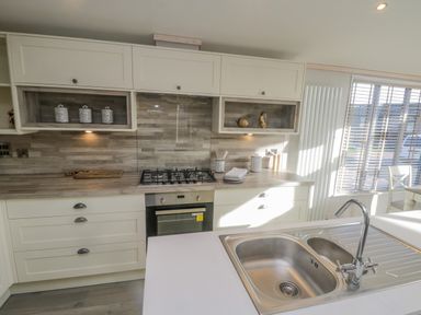 A kitchen with a gas stove oven a double sink countertop and windows with blinds at No 27 The Crab Pot in Runswick Bay near Staithes